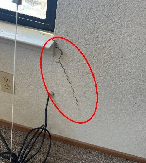 Marked interior wall crack below a window near the localized floor elevation change