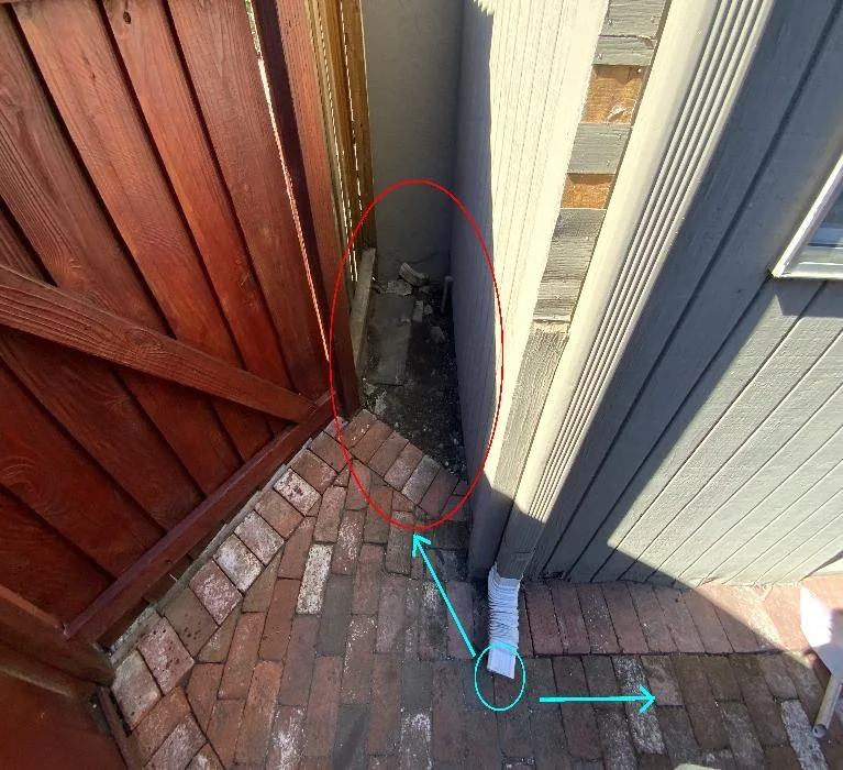 Downspout terminating beside the foundation at the lowest exterior corner of the Pleasanton home
