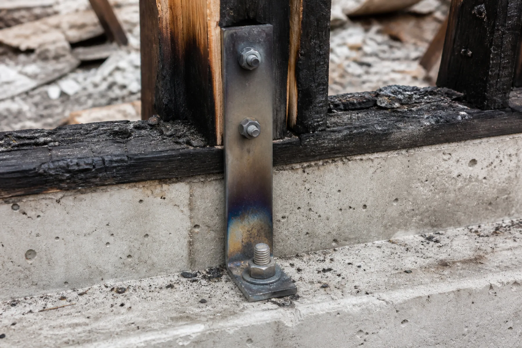 Heat-discolored hold-down and anchor bolt at a burned wall base